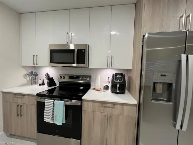 Kitchen featuring stainless steel appliances, tasteful backsplash, modern cabinets, light stone countertops, and white cabinetry