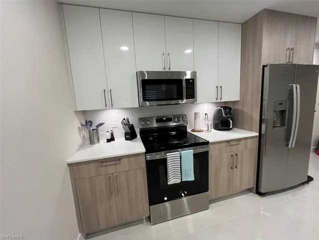 Kitchen with stainless steel appliances, backsplash, modern cabinets, and light tile patterned flooring