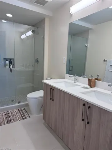 Bathroom with an enclosed shower, vanity, tile patterned floors, and toilet