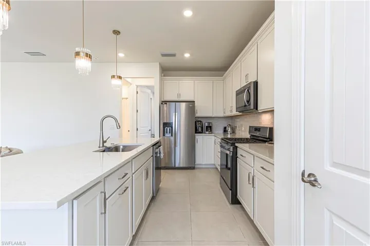 Kitchen with stainless steel appliances, a sink, backsplash, light tile patterned floors, and white cabinetry
