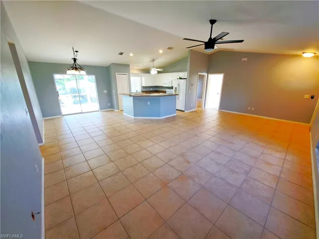 Unfurnished living room featuring ceiling fan with notable chandelier, light tile patterned flooring, and vaulted ceiling