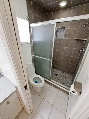 Master Bath shower with door, tile patterned flooring, and toilet