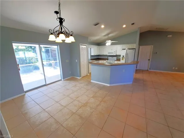Kitchen with white cabinets, white appliances, light tile patterned floors, and vaulted ceiling