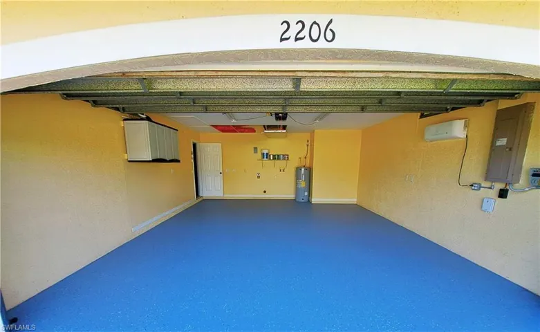 Refinished garage with electric water heater, electric panel, and a wall mounted air conditioner