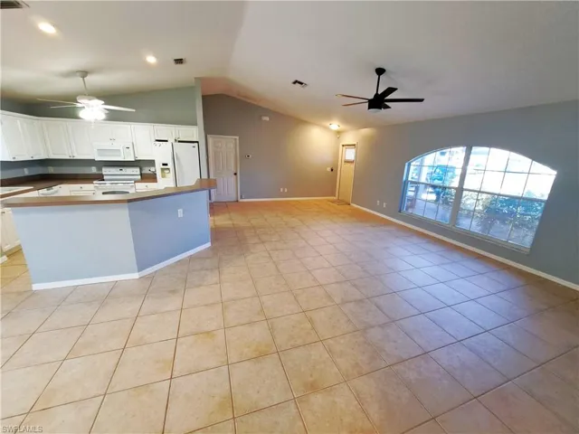 Kitchen featuring white cabinetry, light tile patterned floors, vaulted ceiling, white appliances, and ceiling fan