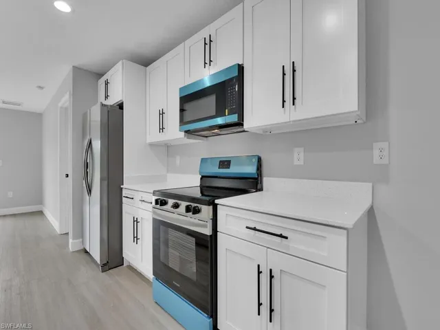 Kitchen with appliances with stainless steel finishes, white cabinets, and light hardwood / wood-style flooring