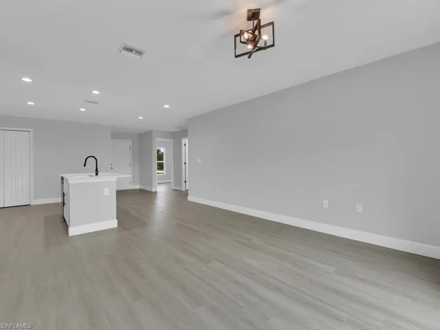 Unfurnished living room with an inviting chandelier, sink, and light hardwood / wood-style flooring