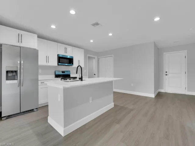 Kitchen featuring stainless steel appliances, an island with sink, and white cabinets