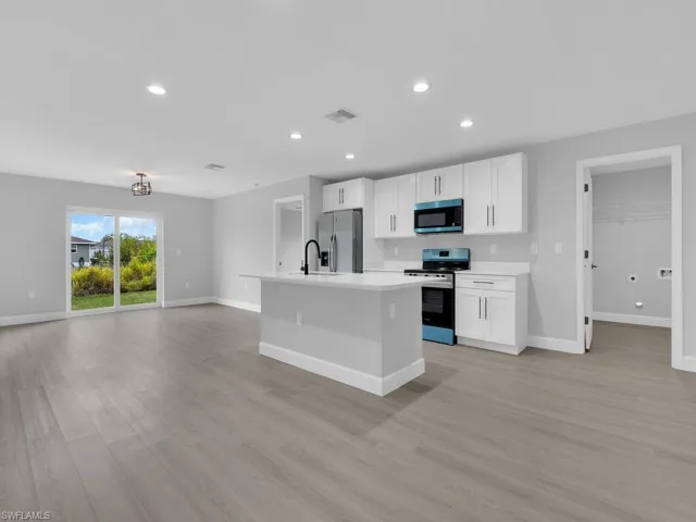 Kitchen with sink, light hardwood / wood-style flooring, stainless steel appliances, an island with sink, and white cabinets