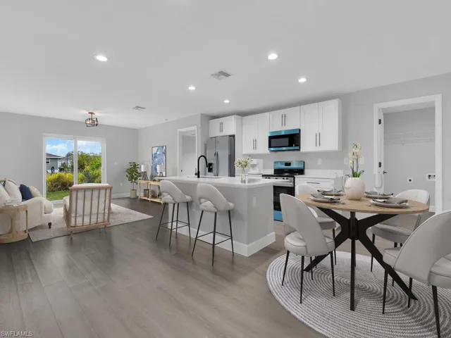 Kitchen with a breakfast bar, stainless steel appliances, light hardwood / wood-style floors, white cabinets, and a center island with sink