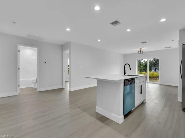 Kitchen featuring sink, white cabinetry, stainless steel dishwasher, an island with sink, and light hardwood / wood-style floors