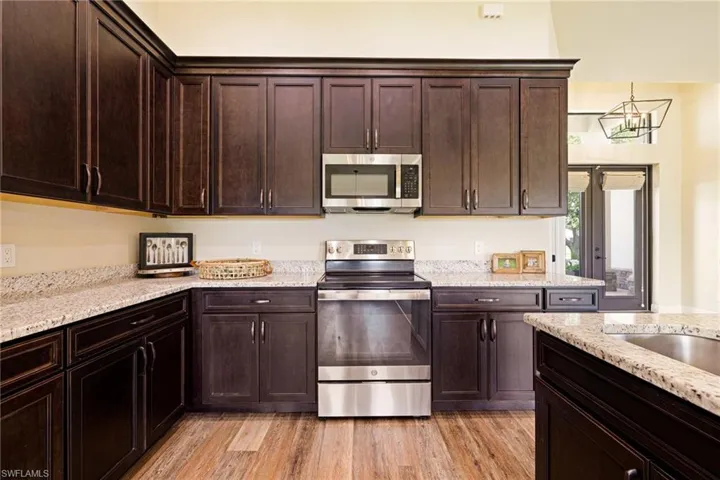 Kitchen with stainless steel appliances, dark brown cabinets, light wood-style floors, and light stone counters