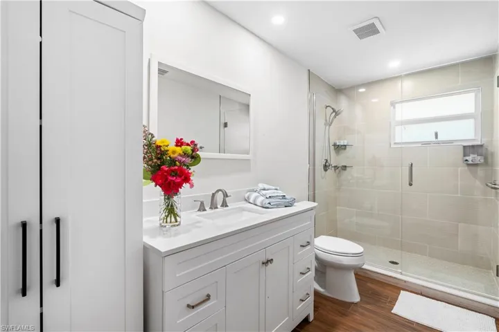 Bathroom with hardwood / wood-style flooring, vanity, toilet, and a shower with door