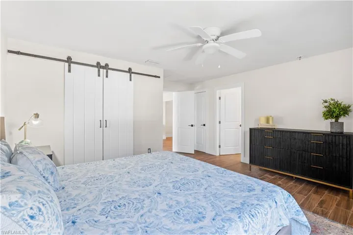 Bedroom featuring dark hardwood / wood-style flooring, a barn door, and ceiling fan