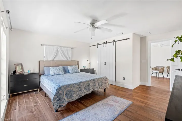 Bedroom with dark wood-type flooring, ceiling fan, and a barn door