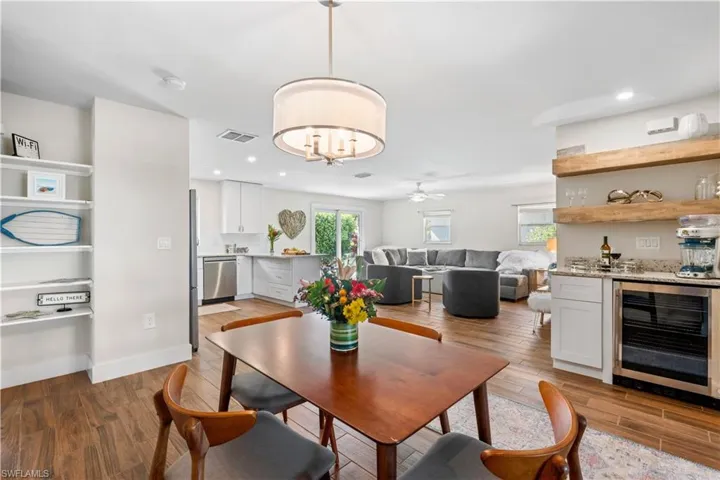 Dining area with ceiling fan with notable chandelier, bar, wine cooler, and light wood-type flooring