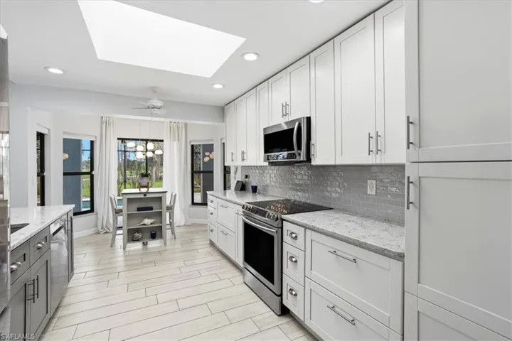 Kitchen with light stone countertops, a breakfast bar area, stainless steel appliances, a skylight, and a ceiling fan