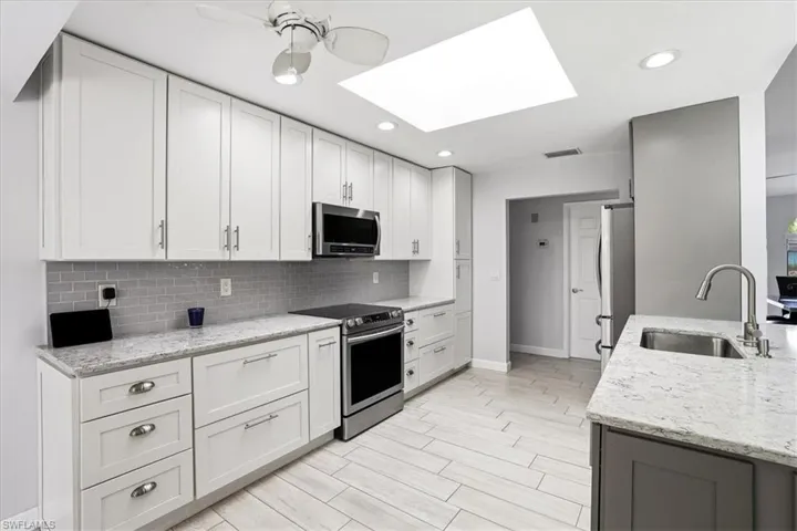 Kitchen featuring stainless steel appliances, a skylight, light stone countertops, wood finish floors, and recessed lighting
