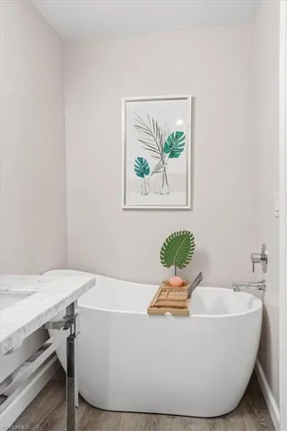 Bathroom with a closet, a freestanding tub, wood finished floors, and wallpapered walls
