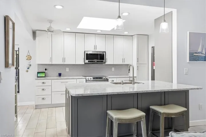 Kitchen with light stone countertops, a breakfast bar area, stainless steel appliances, a skylight, and a ceiling fan