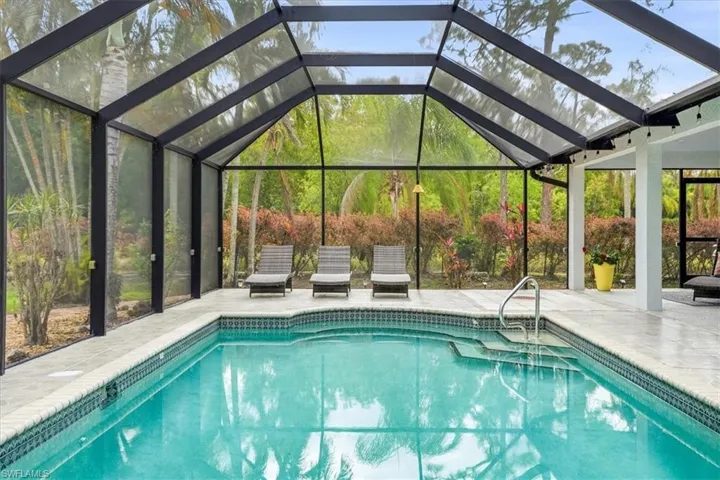 Swimming pool featuring glass enclosure, a patio area, and a sunroom
