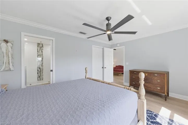 Bedroom with ornamental molding, ceiling fan, light wood-style flooring, and ensuite bathroom
