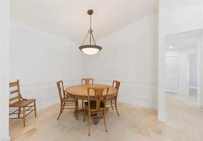 Dining space with lofted ceiling, wainscoting, light stone finish floors, and a decorative wall