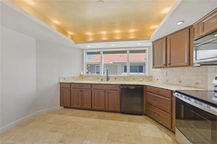 Kitchen with stainless steel range with electric cooktop, a tray ceiling, light stone counters, black dishwasher, and wood finish cabinets