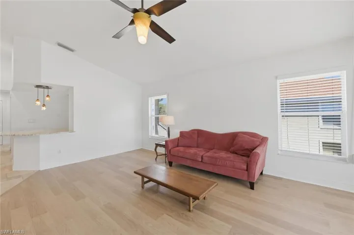 Living room with light wood-style flooring, a ceiling fan, and lofted ceiling