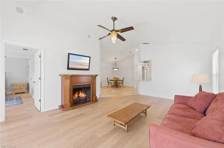 Living room featuring light wood-style floors, ceiling fan, a glass covered fireplace, and vaulted ceiling