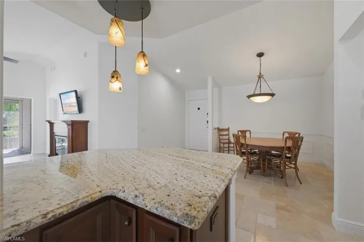 Kitchen featuring dark wood finish cabinets, light stone counters, stone tile flooring, hanging light fixtures, and lofted ceiling