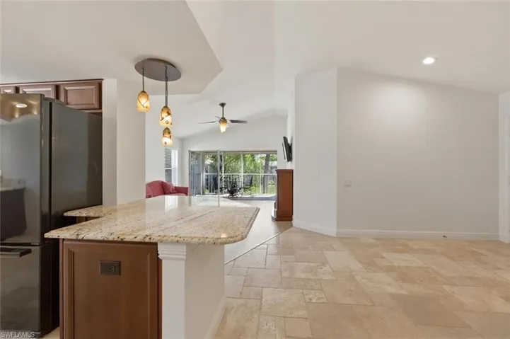 Kitchen with light stone countertops, freestanding refrigerator, open floor plan, ceiling fan, and stone tile flooring