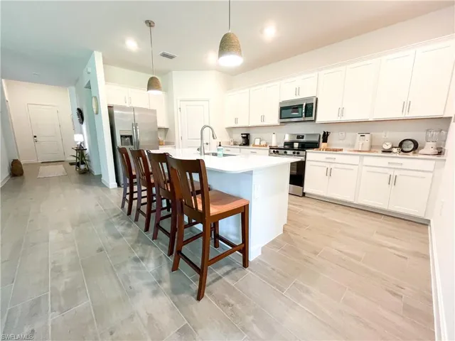 Kitchen featuring stainless steel appliances, light tile-style floors, a kitchen bar, an island with sink, and light countertops