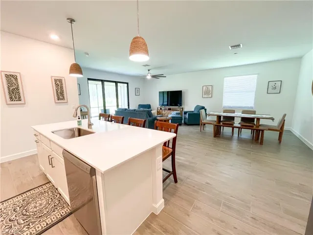 Kitchen featuring dishwasher, hanging light fixtures, a center island with sink, light countertops, and white cabinetry