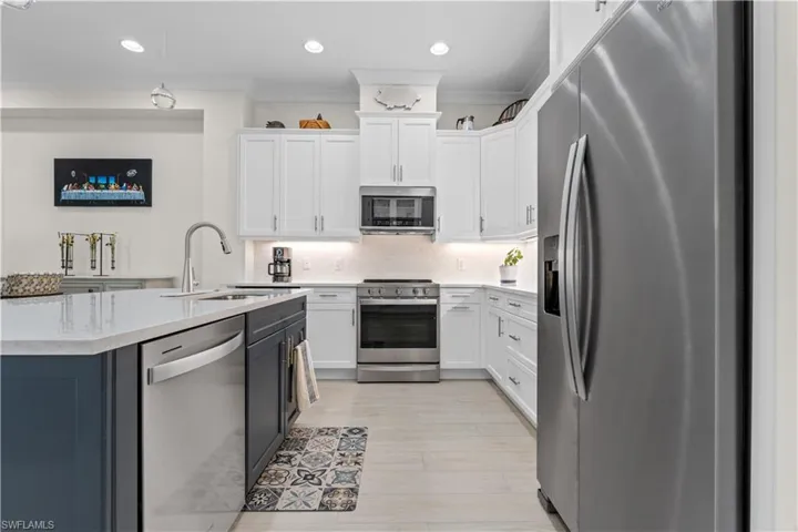 Dual tone kitchen featuring stainless steel appliances, two tone cabinetry, ornamental molding, light stone countertops, and decorative backsplash