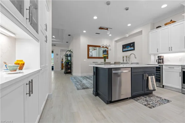 Kitchen with crown molding, light stone countertops, two tone color scheme, stainless steel dishwasher, and a center island with sink