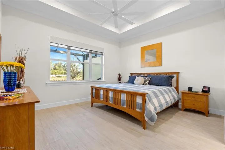 Bedroom featuring light wood-style floors, a ceiling fan, and a raised ceiling