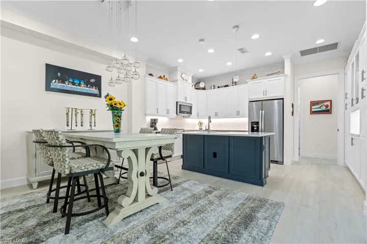 Dual tone kitchen featuring two tone cabinetry, stainless steel appliances, hanging light fixtures, light wood-type flooring, and a kitchen island with sink