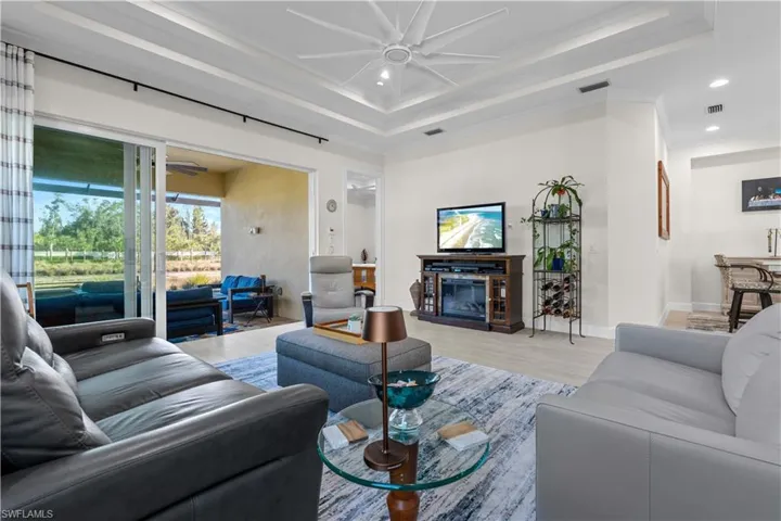 Living room with a ceiling fan, light wood finished floors, a glass covered fireplace, recessed lighting, and a raised ceiling