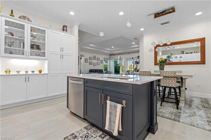 Dual tone kitchen featuring two tone cabinets, light stone counters, an island with sink, pendant lighting, and stainless steel dishwasher