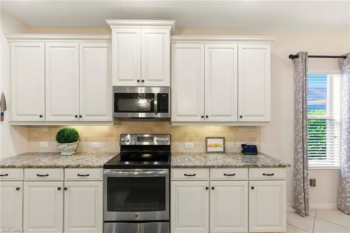 Kitchen with stainless steel appliances, light stone counters, white cabinets, decorative backsplash, and light tile diagonal floors