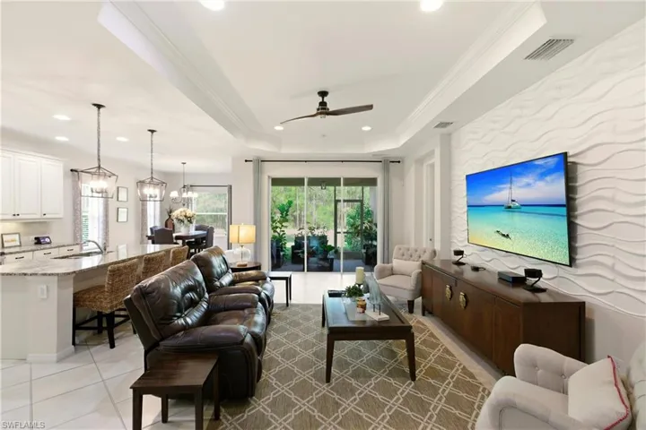 Living room featuring light diagonal tile flooring, tray ceiling, a ceiling fan, crown molding, chandeliers, and recessed lighting