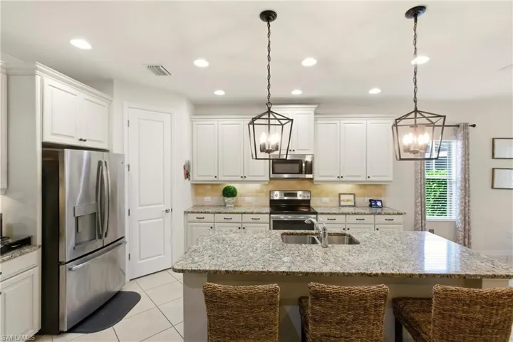 Kitchen with stainless steel appliances, a center island with sink, light stone countertops, a kitchen bar, and light tile diagonal flooring