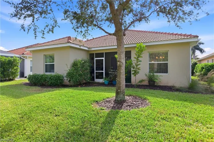 Rear view of property featuring stucco siding, a tile roof, a lanai, and a lawn