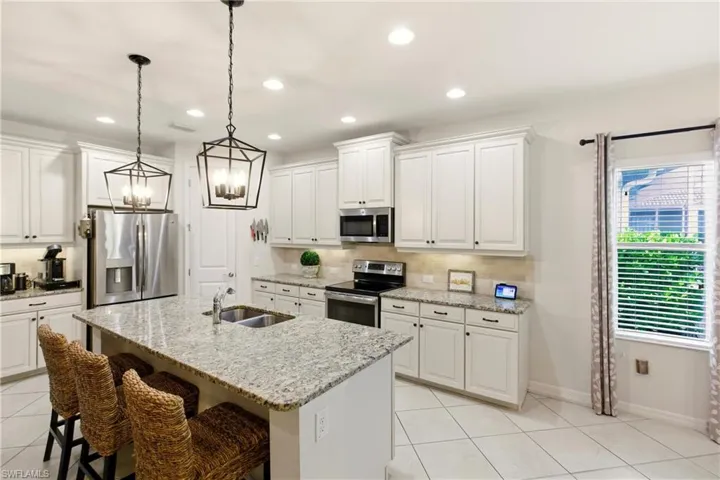 Kitchen with stainless steel appliances, light tile diagonal flooring, white cabinets, light stone countertops, and recessed lighting