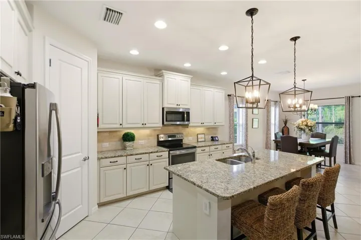 Kitchen featuring stainless steel appliances, light tile diagonal floors, recessed lighting, light stone counters, and hanging light fixtures