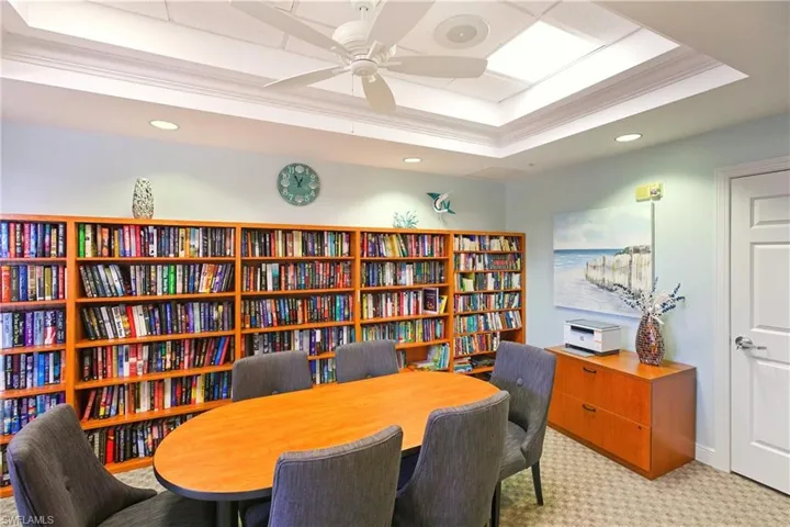 Clubhouse Library/Office featuring crown molding, a raised ceiling, light carpet, wall of books, and ceiling fan