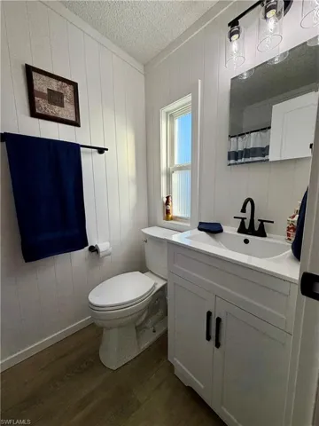 Bathroom featuring vanity, a textured ceiling, wooden walls, hardwood / wood-style flooring, and toilet
