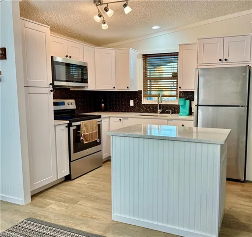 Kitchen with stainless steel appliances, white cabinetry, a kitchen island, and sink