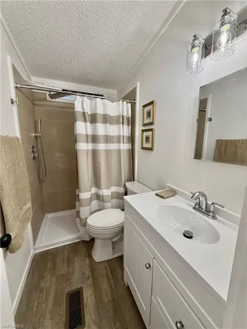 Bathroom with walk in shower, vanity, a textured ceiling, wood-type flooring, and toilet